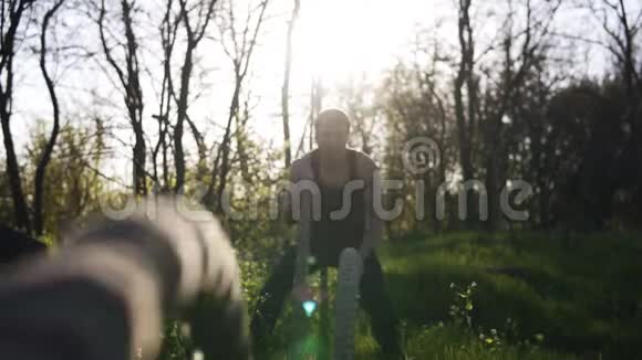 肌肉男用交叉绳索做波浪波斯克背景上的太阳光前方视野靠近绳索视频的预览图