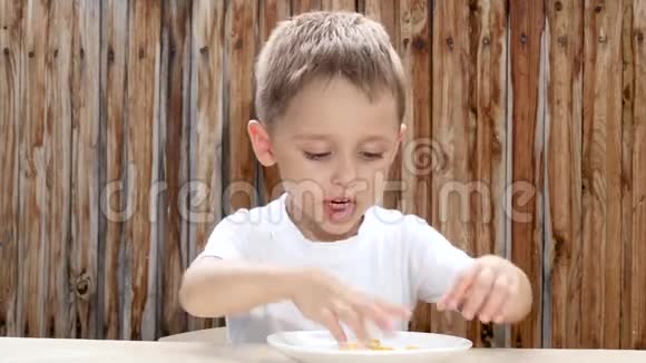 孩子坐在木墙背景的桌子旁高兴地吃薯片视频的预览图