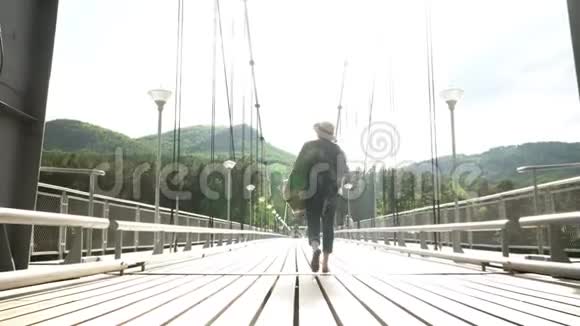 那个穿着斗篷和草帽的女人沿着斜拉桥穿过山河视频的预览图