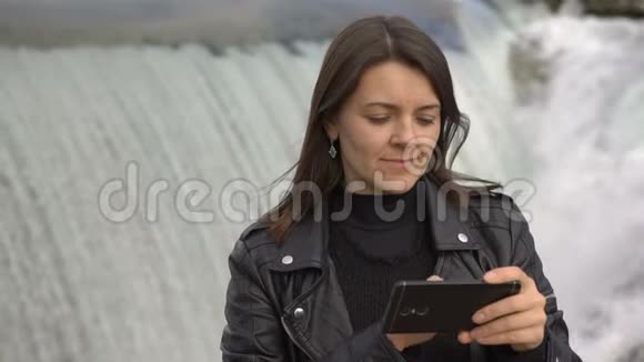 美丽的女人用智能手机视频聊天瀑布背景视频的预览图