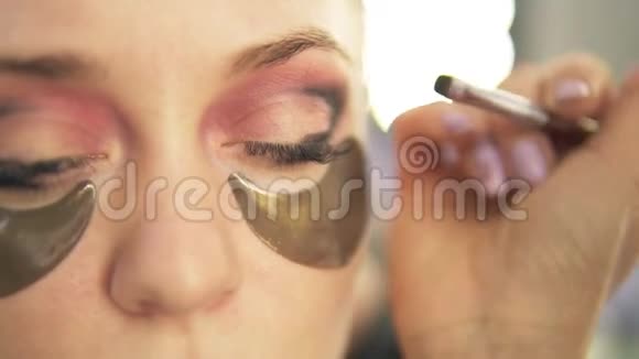 化妆师把阴影放在眼皮上轻发模特关闭视野烟熏的眼睛眼睛下面的金色斑点视频的预览图