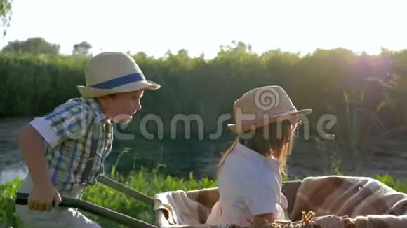 孩子们和小女孩在乡下的手推车里跑步孩子们戴着草帽在湖边玩得很开心视频的预览图