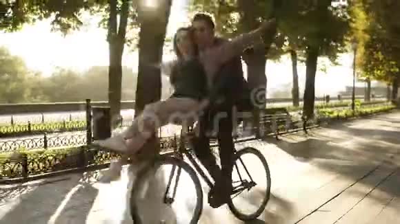 年轻夫妇在户外活动中骑在同一辆自行车上玩得很开心背景是太阳背光坐着的女孩视频的预览图