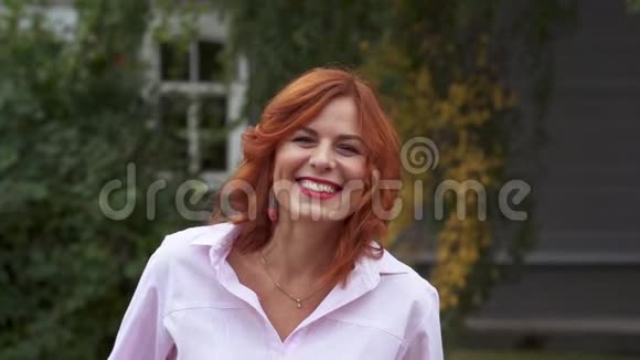 一位留着红色长发和粉红色衬衫的中年妇女正在微笑视频的预览图