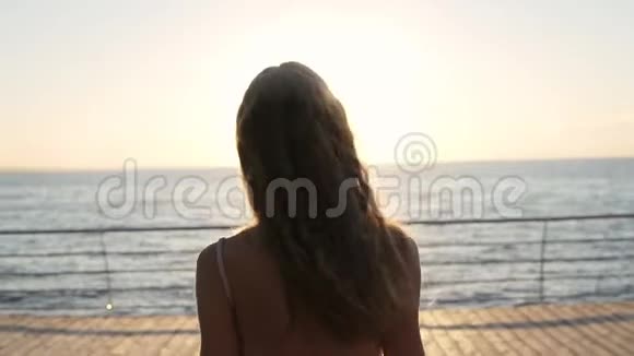 年轻女子举起双手缓慢地走在海边背景下窈窕淑女阳光明媚视频的预览图