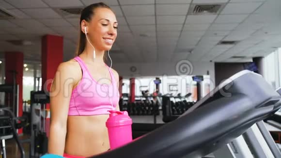年轻女子在健身俱乐部的跑步机上训练和喝蛋白质奶昔视频的预览图