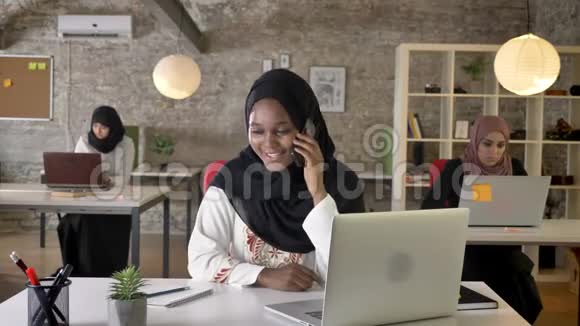 年轻的穆斯林黑人妇女戴着头巾在办公室里谈笑风生三个漂亮的穆斯林妇女在工作视频的预览图