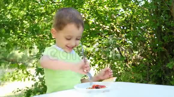 孩子在大自然的背景下坐在一张桌子旁吃着一个什什锦串用番茄酱烧烤视频的预览图