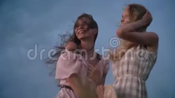 两个年轻迷人的女孩子穿着连衣裙迎风招展夏天雨天在田间抚摸头发自由的概念视频的预览图