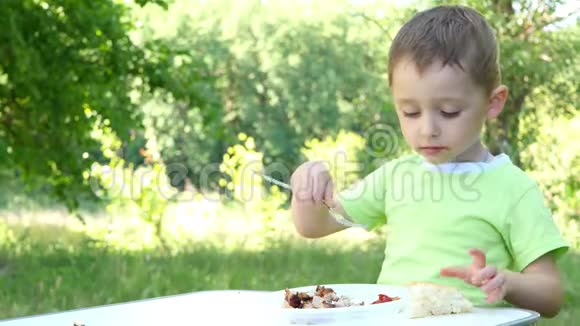 一个拿着叉子的孩子吃着什锦串烧烤坐在大自然的桌子旁视频的预览图