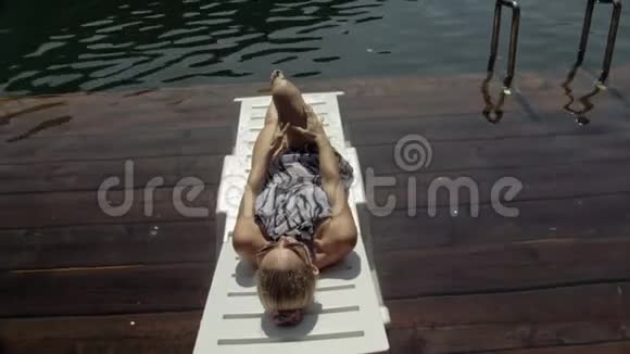 女人躺在太阳床上戴着太阳镜和一条薄纱披肩女孩在洪水木水下码头休息路面是视频的预览图