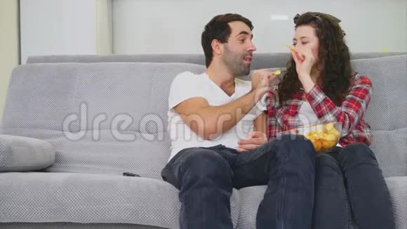 微笑的妻子和男人坐在沙发上在这期间看电视把筹码给对方穿着黑色牛仔布视频的预览图