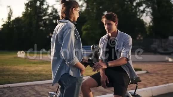 年轻夫妇穿着同样的蓝色衬衫在街上闲逛男孩坐在电动自行车上打手势和他说话视频的预览图