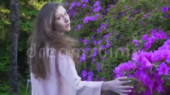 女孩走过一个鲜花盛开的大花坛看着镜头视频的预览图