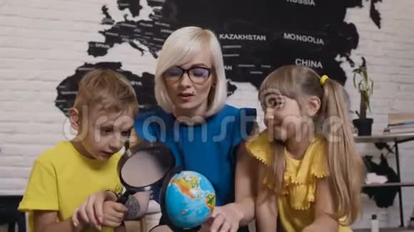 两个可爱的小学生和年轻的老师戴着眼镜手里拿着头皮屑有趣地研究地球的画像视频的预览图