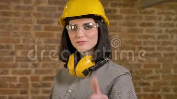 年轻漂亮的建筑女工站着看着镜头竖起大拇指微笑着带着砖块背景盘旋着视频的预览图