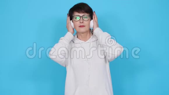 热爱音乐的理念成熟的女人用蓝色背景的耳机播放音乐视频的预览图