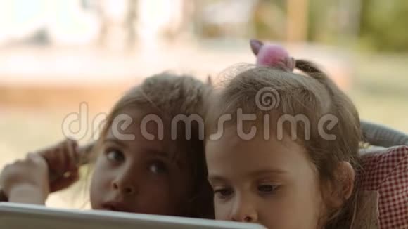 可爱的姐妹们拿着平板电脑看着上面的卡通视频的预览图
