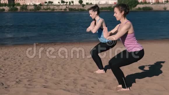两个女人在城市河边的海滩上做瑜伽美丽的景色尤卡塔萨纳姿势视频的预览图
