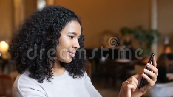 年轻的非洲裔美国黑人妇女在咖啡馆玩智能手机技术视频的预览图