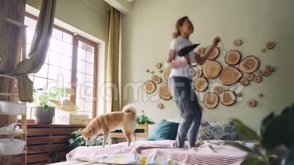有趣的非裔美国女孩正在享受音乐的乐趣在床上跳跃和跳舞用吹风机唱歌视频的预览图