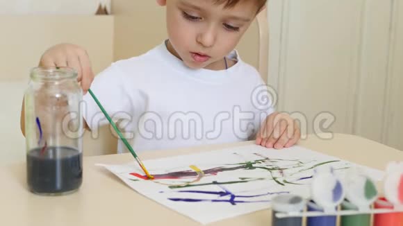 一个孩子男孩在一张白纸上画水彩画一个孩子坐在桌子旁画画视频的预览图