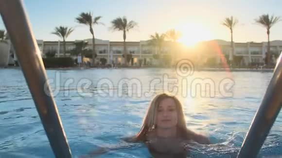 在炎热的阳光明媚的日子里从蓝色的游泳池里拿出一幅迷人的年轻女人的肖像比基尼视频的预览图