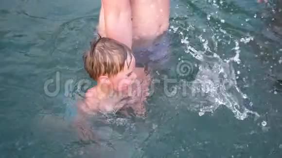 一位年轻的爸爸和他的孩子在炎热的夏天在一个小湖里游泳这孩子非常快乐和快乐花园鲜花视频的预览图