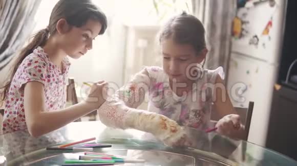 孩子们用绷带把一只涂满石膏的手臂画在一起姐姐鼓励和照顾生病的妹妹视频的预览图