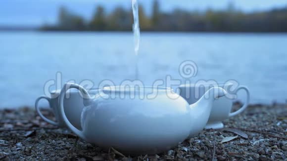 特写镜头一股沸水涌入一只白瓷茶壶它矗立在石质河岸上视频的预览图