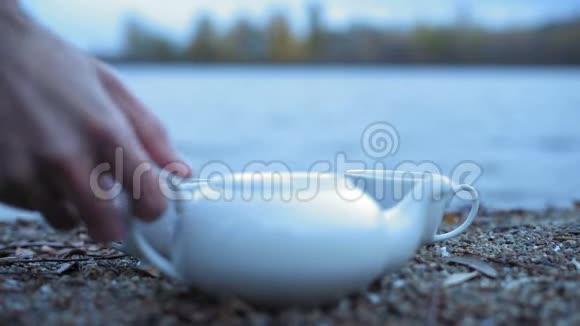 在石河畔的立杯中男子亲手从白瓷茶壶中倒入绿茶视频的预览图