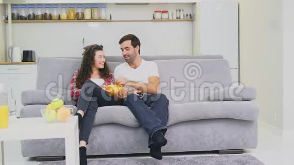 微笑的妻子和男人坐在沙发上看这台电视用嘴唇握住你的芯片看着相机视频的预览图