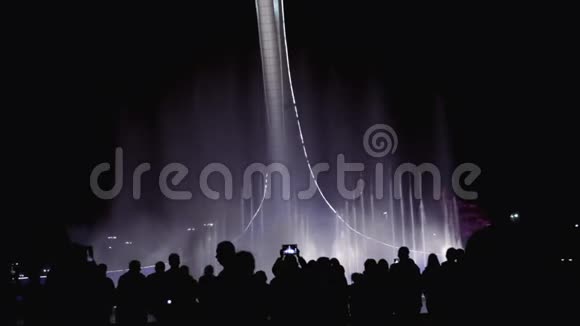 一群人欣赏城市夜景和灯光音乐喷泉表演背景上的人轮廓鲜明视频的预览图