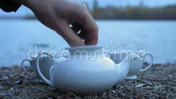 雄手特写将绿茶倒入河畔的白瓷茶壶中视频的预览图