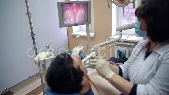 一位女牙医用口腔内摄像机检查一位病人的牙齿并将结果显示在监视器上治疗视频的预览图