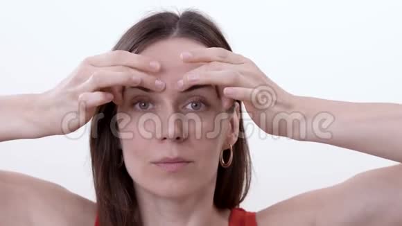 在眉毛上做手指水平移动以减少眉毛之间的皱纹的深色女人的特写视频的预览图