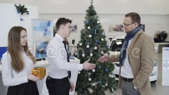在圣诞树的背景下男人们在漂亮的汽车经销店里握手视频的预览图
