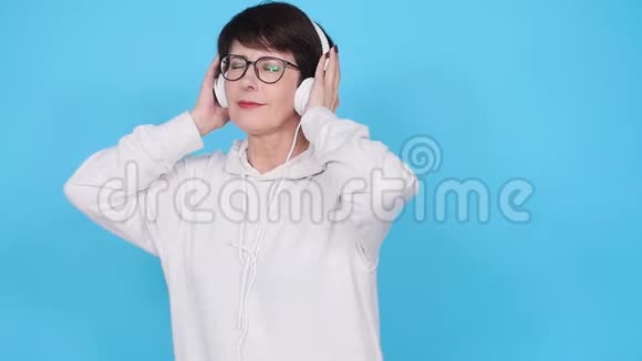 热爱音乐的理念成熟的女人用蓝色背景的耳机播放音乐视频的预览图
