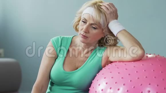 老年女性靠在健身球上用毛巾扇自己精疲力竭视频的预览图
