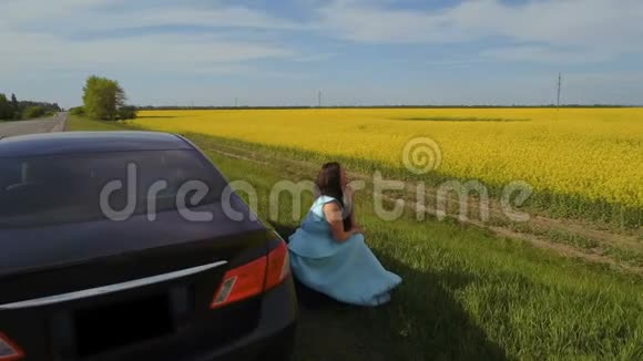 年轻女子坐在车旁的路边欣赏美丽的油菜花田视频的预览图