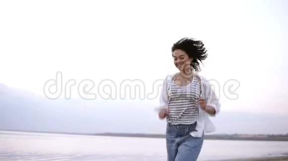 年轻快乐开朗的黑发女孩快乐地穿着便服在海边跑步自由健康的生活方式视频的预览图