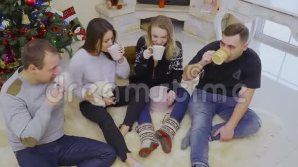 四个年轻人坐在圣诞树附近的地板上喝茶或咖啡视频的预览图