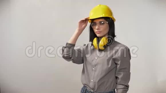 年轻建筑工人妇女戴着耳机眼镜和头盔戴着头盔表情严肃背景白色视频的预览图