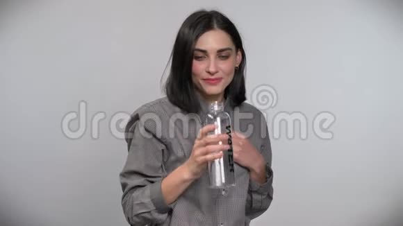 年轻的美女一头棕色短发从瓶子里喝着水微笑着白色的背景视频的预览图