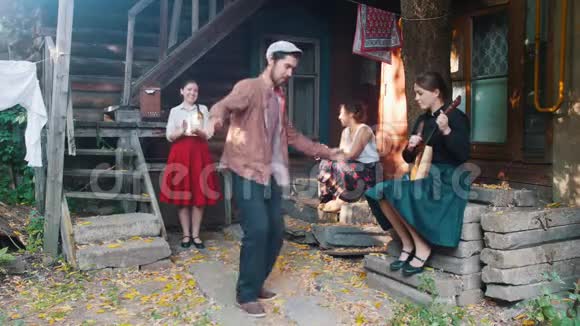 一个男人在跳俄罗斯民族舞蹈一个女人坐在乡间别墅附近的楼梯上看着他一个女人在玩视频的预览图