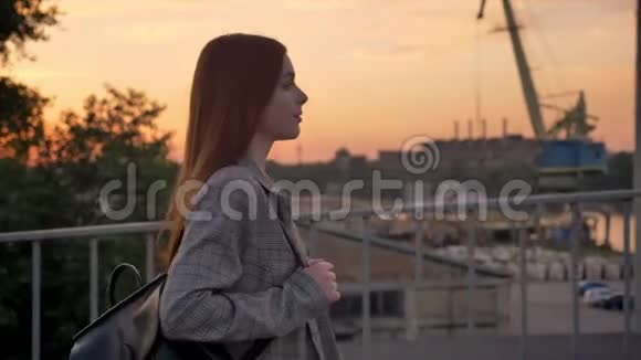 年轻的姜女穿着夹克走过桥工业工厂背景日落视频的预览图