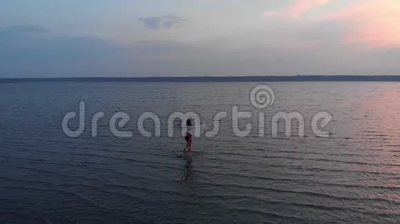 日落时分湖中一个女孩的剪影美丽的女孩独自在浅水中摆姿势轻波荡漾视频的预览图