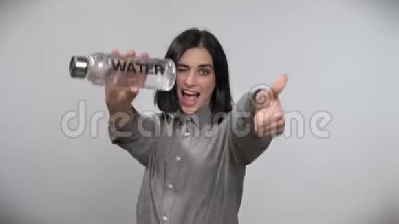 年轻漂亮的女人留着短发拿着水指着瓶子大拇指照相机微笑着白色背景视频的预览图