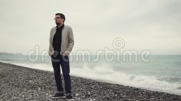 一个戴眼镜的人站在靠近大海的石滩上望着远处视频的预览图