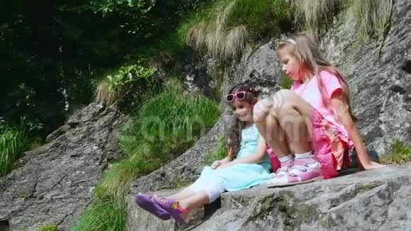 两个漂亮的女孩孩子们坐在岩石的窗台上一只美丽的橙色山蝶旋转着飞过一个孩子视频的预览图